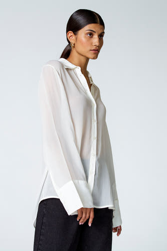 Ecru blouse met lange mouwen van Astrid Black Label, met een knoopsluiting en gedragen met donkere jeans.
