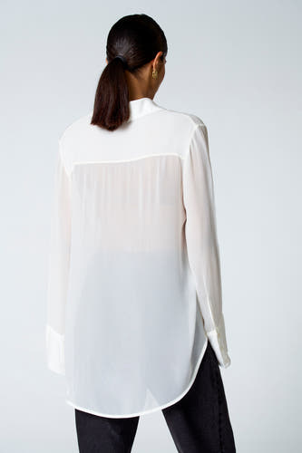 Ecru blouse met lange mouwen van Astrid Black Label, met een semi-transparante stof en een afgeronde zoom aan de achterkant.
