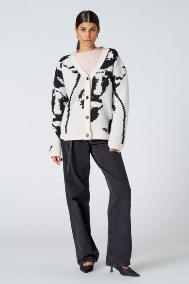 Ecru gilet van Astrid Black Label met een zwart patroon, gedragen over een lichtroze top en zwarte spijkerbroek met hakken.
