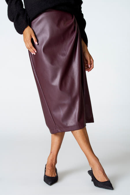 Bordeaux rok van Astrid Black Label, met overslagdetail en gecombineerd met zwarte trui en zwarte pumps.
