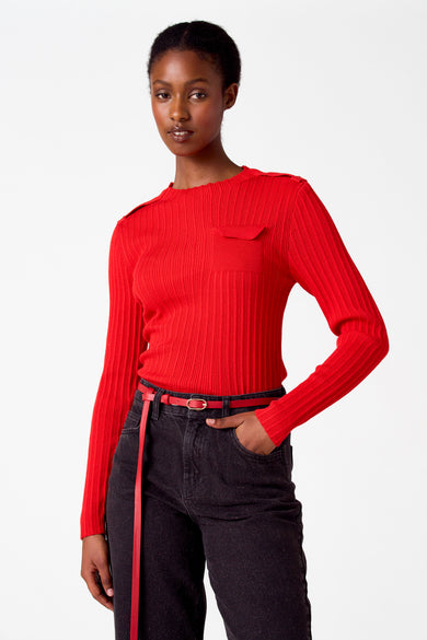 Pull-over rouge à col rond d'Astrid Black Label, avec un motif côtelé, porté avec un jean noir et une ceinture rouge.