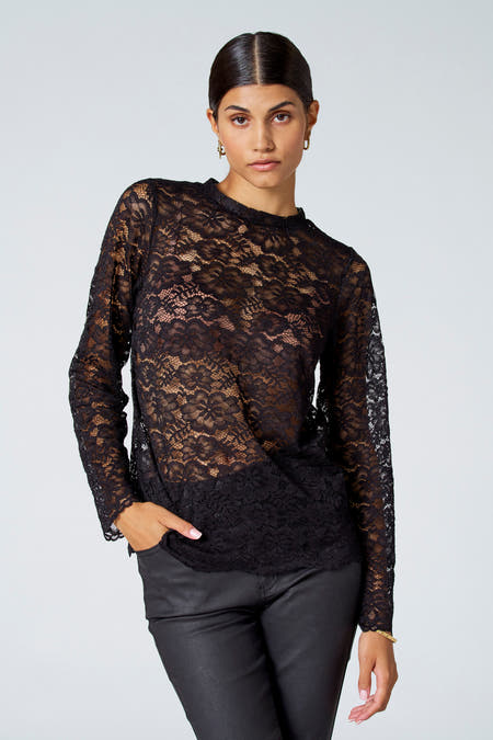 Zwarte blouse met lange mouwen van Astrid Black Label, met kanten bloemmotief en gecombineerd met zwarte broek en gouden oorbellen.
