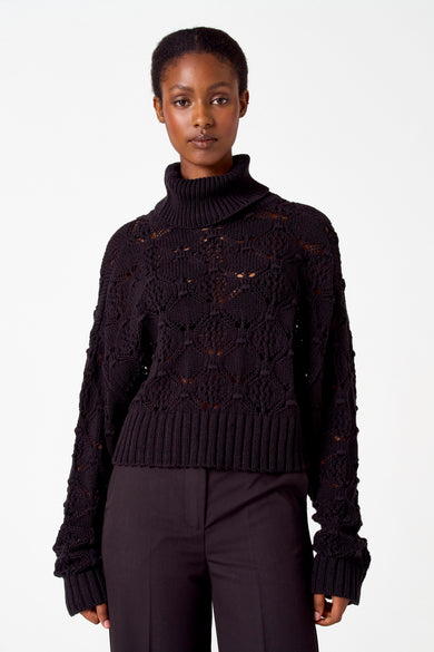 Zwarte trui met rolkraag van Astrid Black Label, met ajourpatroon en gedragen met een zwarte pantalon.
