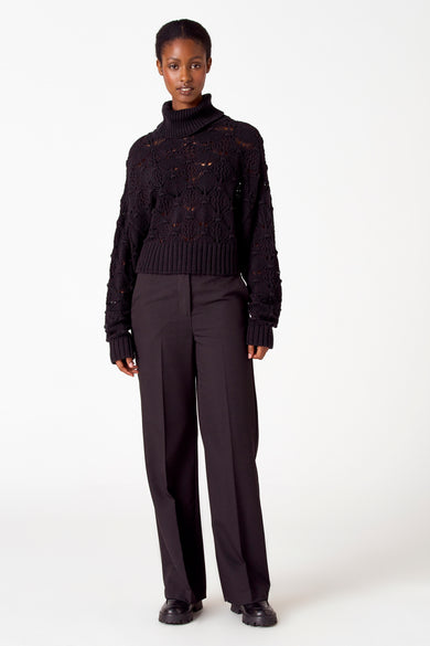 Zwarte trui met rolkraag van Astrid Black Label, met ajourpatroon en ribgebreide boorden, gecombineerd met pantalon en schoenen.

