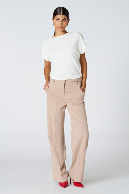T-shirt écru d'Astrid Black Label, porté avec un pantalon kaki et des escarpins rouges, sur un fond blanc.