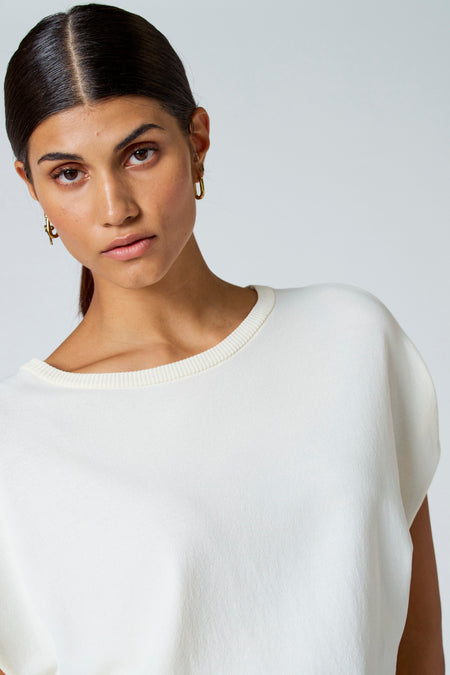 T-shirt écru d'Astrid Black Label, avec une encolure ronde et des boucles d'oreilles dorées.