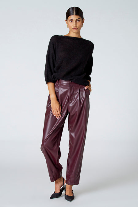Zwarte trui met ronde hals van Astrid Black Label, gecombineerd met bordeauxrode leren broek en zwarte hakken.