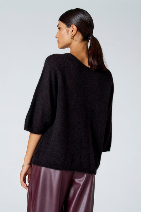 Pull noir à col rond d'Astrid Black Label, vu de dos, avec des manches courtes et porté avec un pantalon en cuir bordeaux.