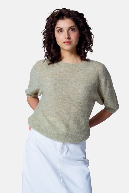 Groene trui met ronde hals van Astrid Black Label, met korte mouwen, gedragen met een witte broek.
