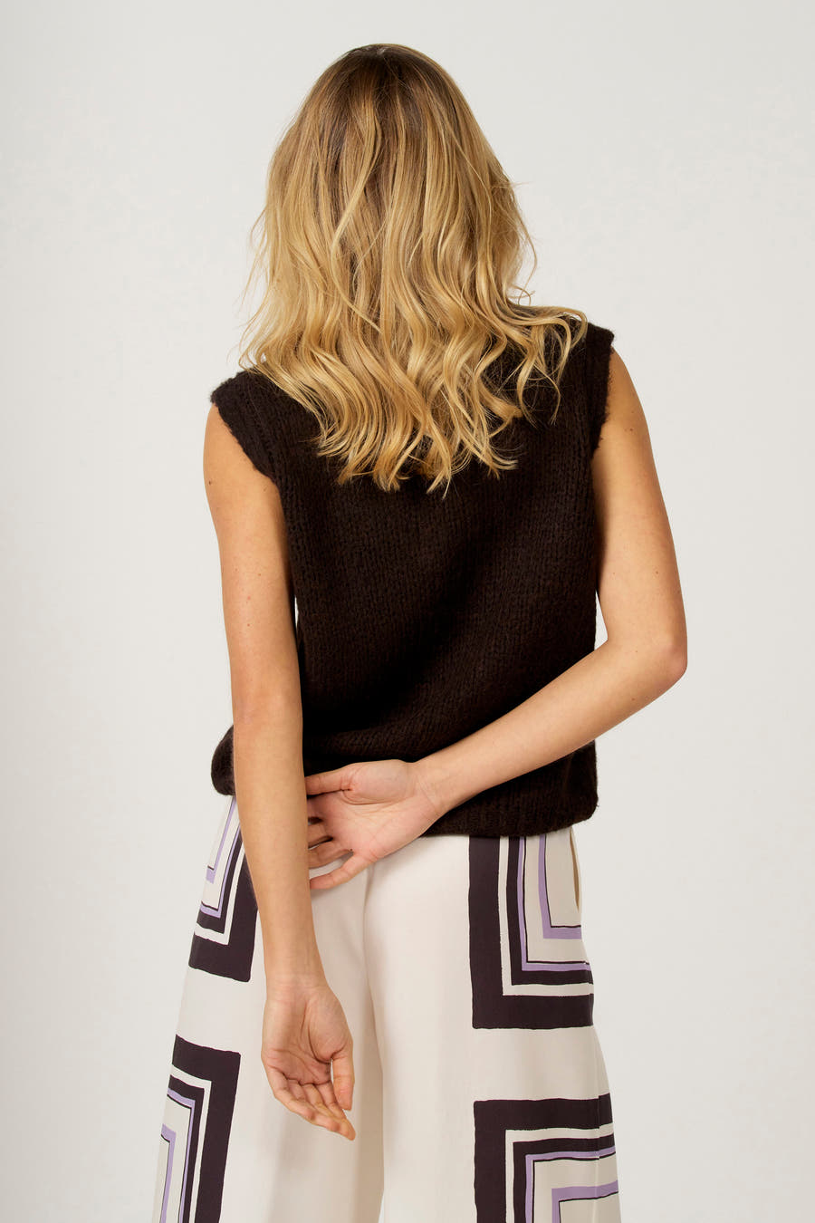 Bruine debardeur van Astrid Black Label, met een grof gebreide textuur, gecombineerd met een crèmekleurige broek met geometrisch patroon.
