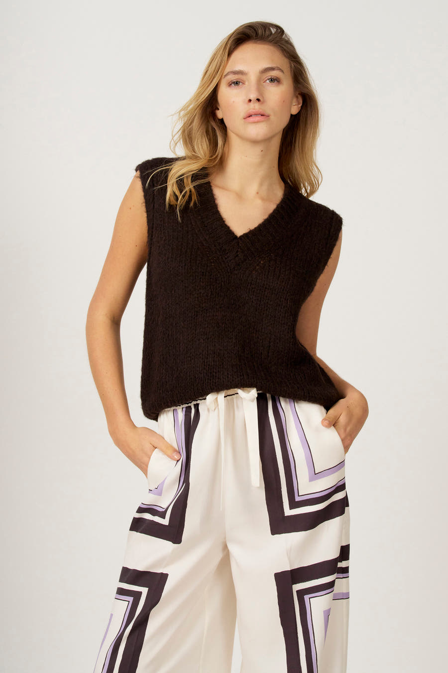 Bruine debardeur van Astrid Black Label, met V-hals, gecombineerd met een witte broek met geometrisch patroon.
