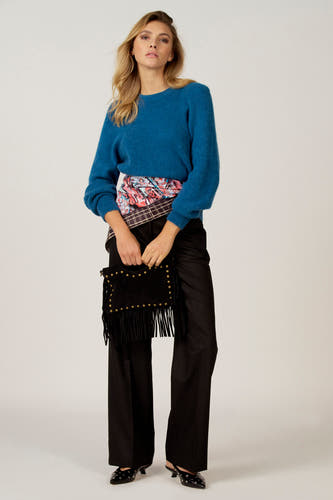 Pantalon noir d'Astrid Black Label, associé à un pull bleu, une poche noire avec des franges et des chaussures noires.