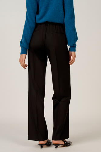 Pantalon noir d'Astrid Black Label, vu de derrière, avec un pull bleu et des escarpins noirs à strass.