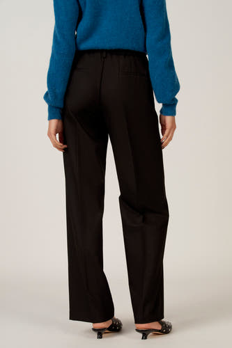 Zwarte broek van Astrid Black Label, met rechte pijpen en steekzakken, gedragen met een blauwe trui en zwarte muiltjes.
