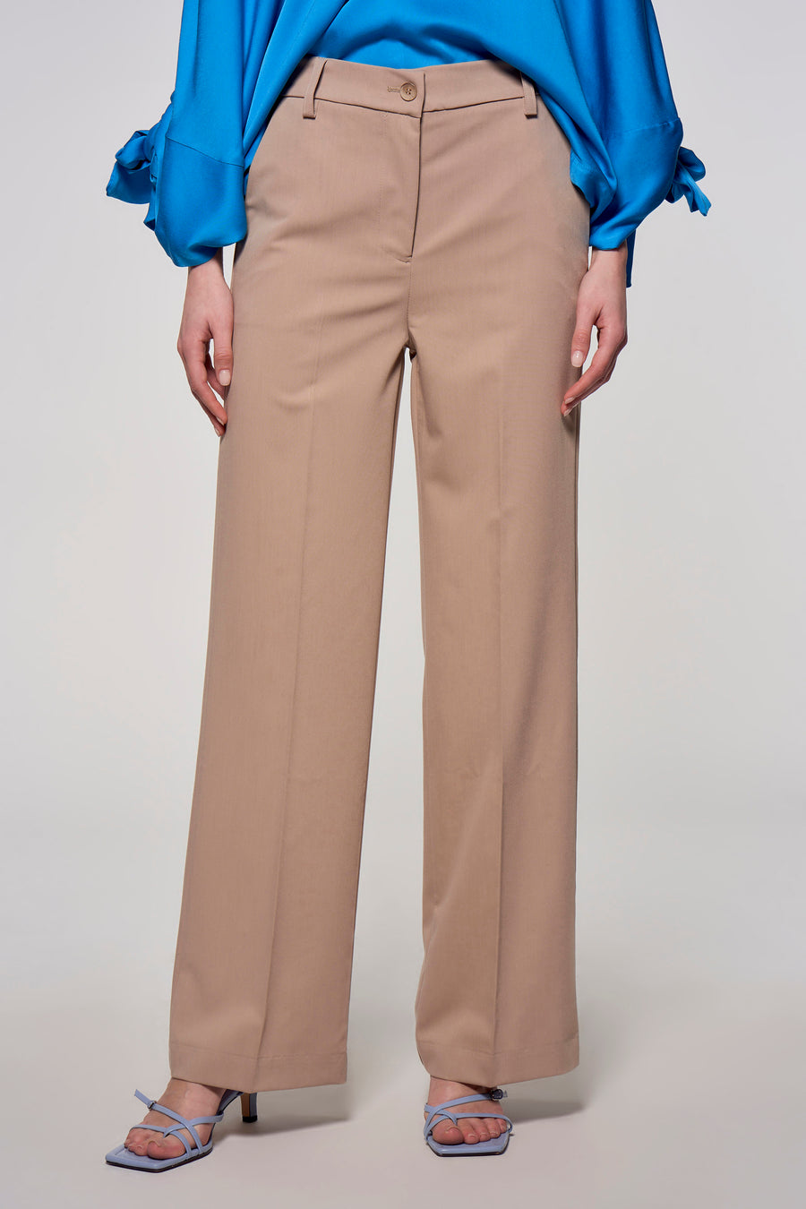 Vrouw draagt beige pantalon met blauwe blouse en sandalen.