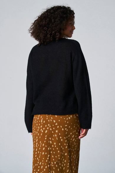 Pull noir avec col rond d'Astrid Black Label, avec des manches longues et une jupe marron à carreaux.