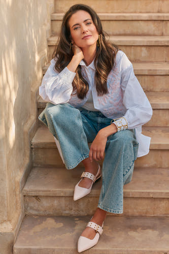 Ballerines roses d'Astrid Black Label, assises sur un escalier, associées à une blouse blanche et des jeans.