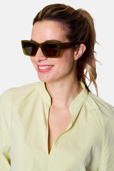 Lunettes de soleil vertes d'Astrid Black Label, avec un cadre carré, portées par une femme en une blouse claire.
