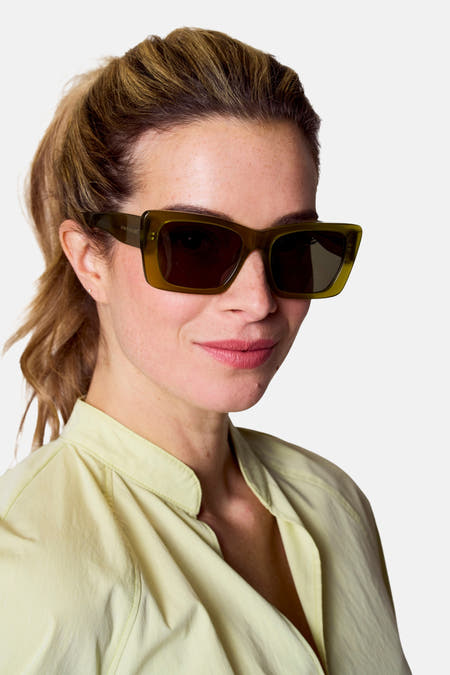 Groene zonnebril van Astrid Black Label, gedragen door een vrouw met een lichtgekleurde blouse en opgestoken haar.
