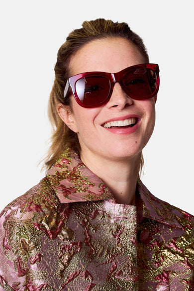 Lunettes de soleil roses d'Astrid Black Label, avec des verres marrons et un cadre anguleux.