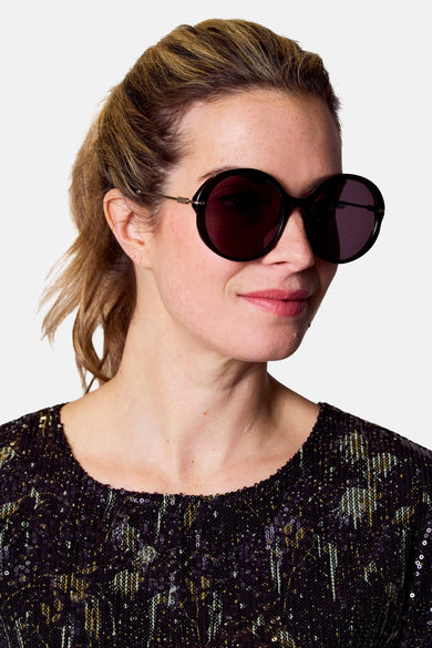 Lunettes de soleil noires d'Astrid Black Label, avec une forme ronde et des détails dorés.
