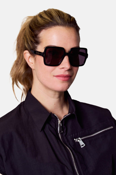 Lunettes de soleil noires d'Astrid Black Label, avec un cadre carré et des détails dorés.