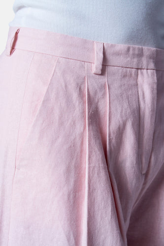 Close-up roze linnen pantalon met plooien en witte ribbeltop.
