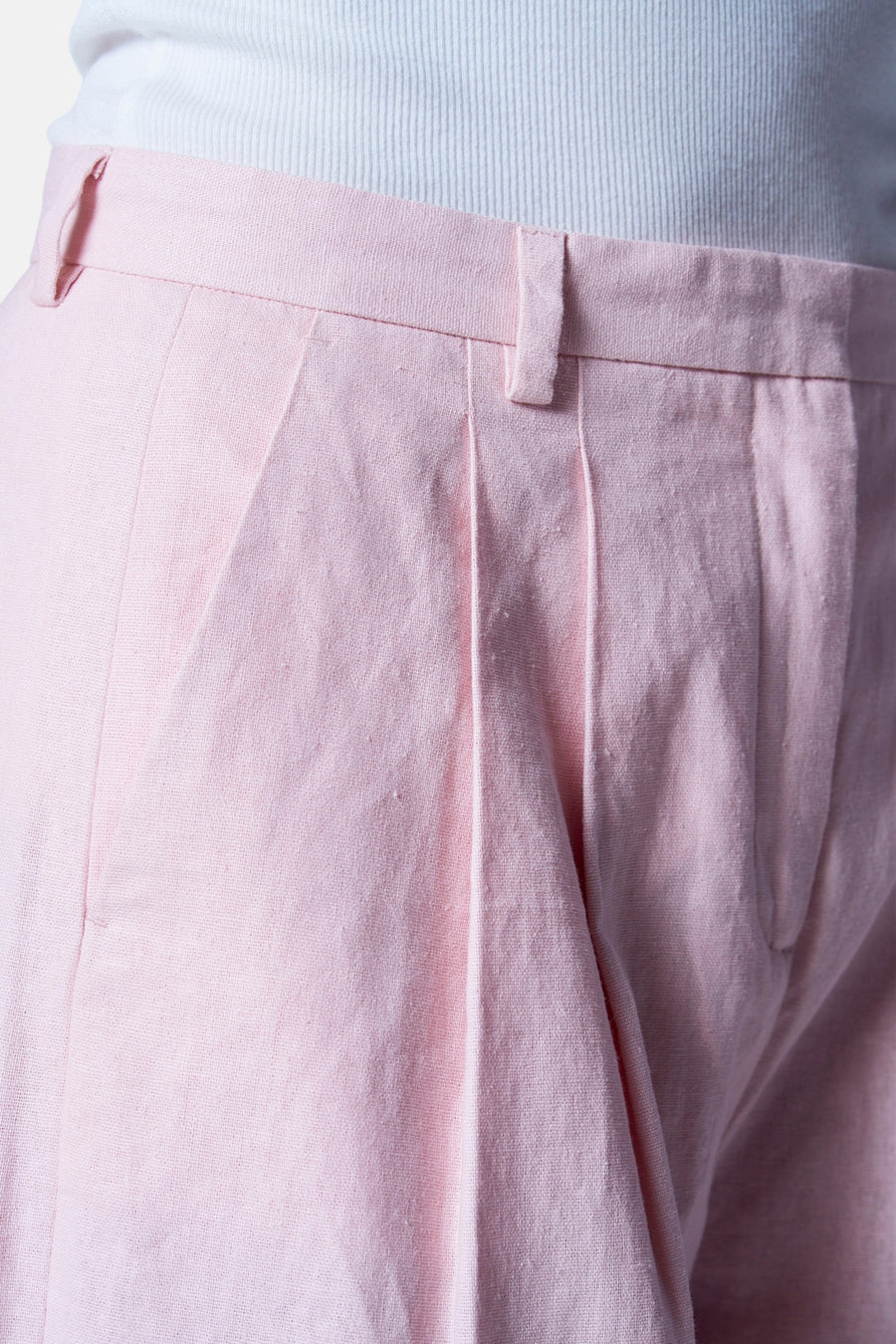 Close-up roze linnen pantalon met plooien en witte ribbeltop.
