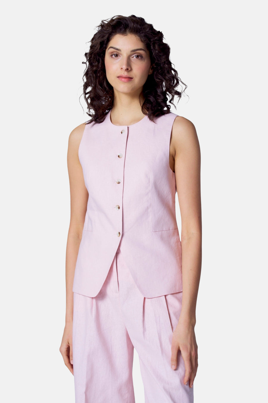 Vrouw in roze linnen pak, vest en pantalon, staand.