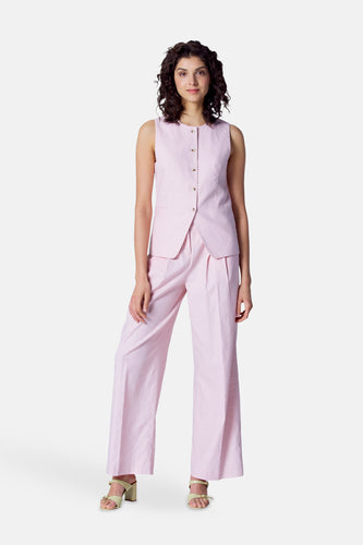 Vrouw in roze broekpak met gilet, beige sandalen.