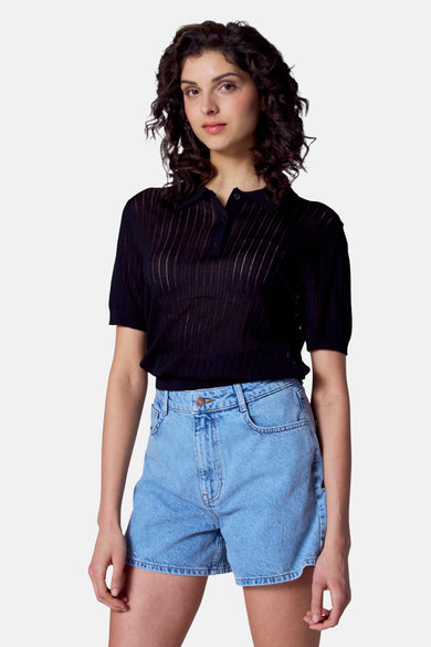 Polo noir à manches courtes d'Astrid Black Label, avec des boutons et porté avec des shorts en denim.