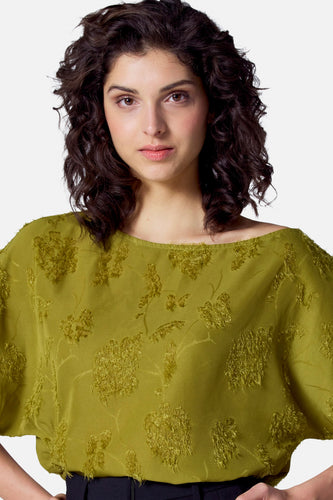 Vrouw in olijfgroene blouse met bloemenpatroon, voor een witte achtergrond.