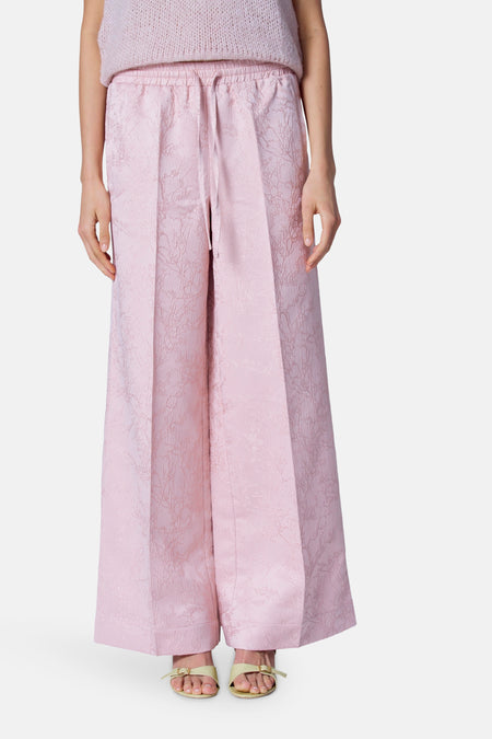 Roze broek van Astrid Black Label met een subtiele textuur en wijde pijpen, gedragen met sandalen.

