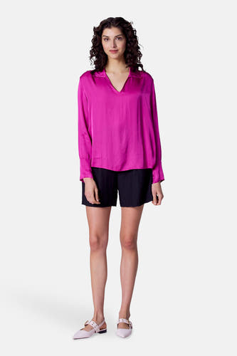 Roze blouse met lange mouwen van Astrid Black Label, met V-hals en gedragen met zwarte shorts en roze schoenen.
