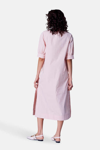 Robe rose à manches courtes d'Astrid Black Label, vue de derrière, avec une fente sur le côté et des chaussures plates coordonnées.