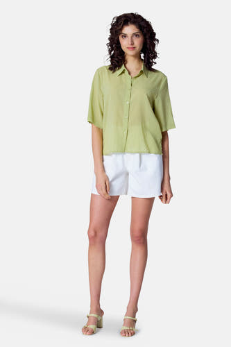 Groene blouse met korte mouwen van Astrid Black Label, met subtiel stippenpatroon, gecombineerd met witte shorts en hakken.