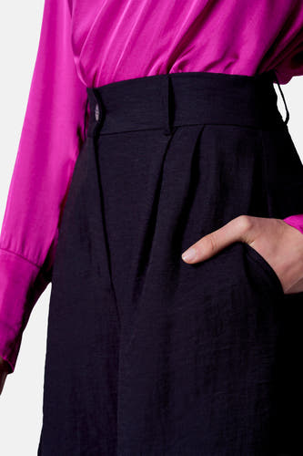 Zwarte short van Astrid Black Label, met een hand in de zak en een magenta satijnen blouse.
