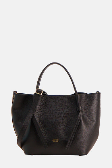 Sac à main noir d'Astrid Black Label, avec texture et une anse, porté avec une blouse blanche et un pantalon beige.