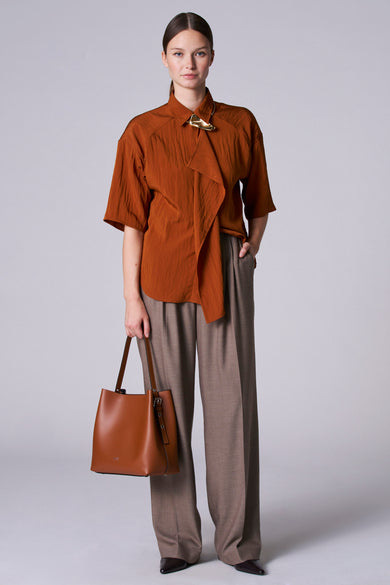 Bruine blouse met driekwartmouwen van Astrid Black Label, met gouden decoratieve sluiting en gedrapeerd detail.