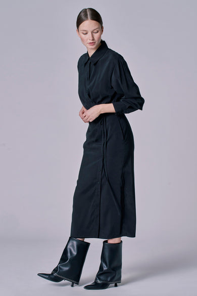 Robe noire à longues manches d'Astrid Black Label, avec une fermeture à boutons et portée avec des bottes noires.