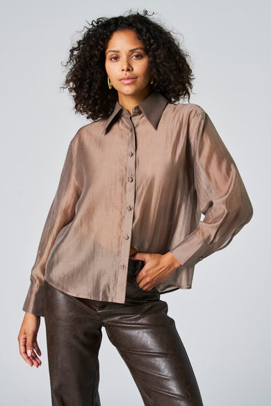 Taupe blouse met lange mouwen van Astrid Black Label, met een doorschijnende textuur, gedragen met bruine leren broek.
