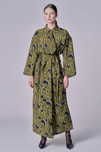 Groene kleedje met lange mouwen van Astrid Black Label, met abstracte print en strikceintuur, gedragen met zwarte panty's en hakken.

