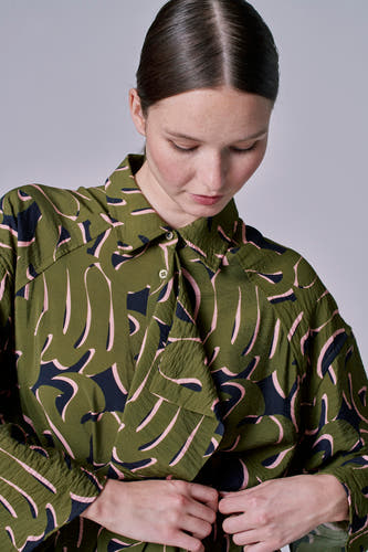 Groene jurk met lange mouwen van Astrid Black Label, met een abstract bladmotief in roze en zwart.
