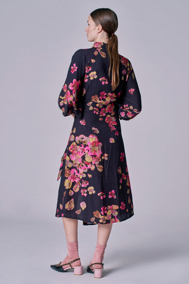 Zwarte jurk met lange mouwen van Astrid Black Label, met roze en gele bloemenprint, losse pasvorm en halfhoge hakken.
