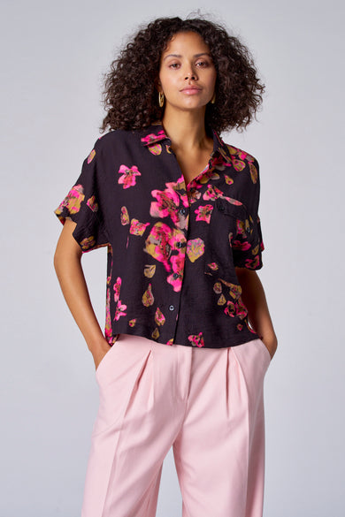 Zwarte blouse met bloemenprint van Astrid Black Label, met korte mouwen en roze pantalon.
