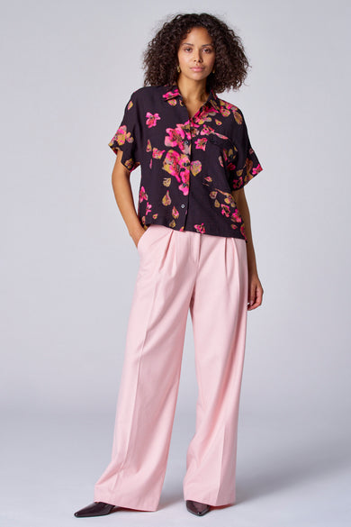 Zwarte blouse met bloemenprint van Astrid Black Label, gedragen met roze, wijde broek en donkere schoenen.
