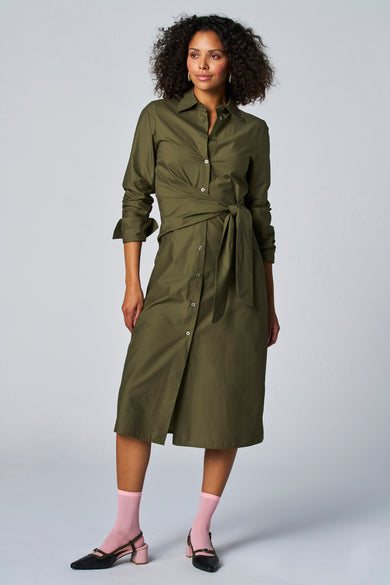 Robe kaki à longues manches d'Astrid Black Label, avec une ceinture nouée à la taille et des chaussettes roses.