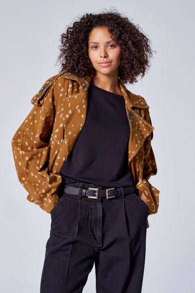 Bruine korte jas van Astrid Black Label, met stippenpatroon, gedragen over een zwarte trui en een donkere broek met dubbele riem.
