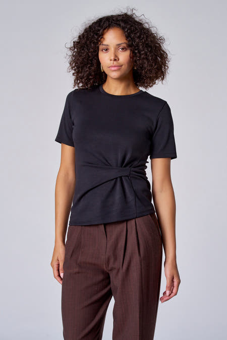 Zwart T-shirt met korte mouwen van Astrid Black Label, met een knoopdetail aan de voorkant, gecombineerd met bruine pantalon.
