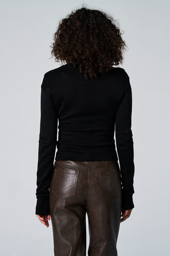 Zwart T-shirt met lange mouwen van Astrid Black Label, met krullend haar en bruin leren broek.
